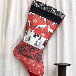 May include: A handmade Christmas stocking with a red fox and snowflake pattern. The stocking features a black and white polka dot cuff and a red hanging loop. The design includes geometric and tree patterns.