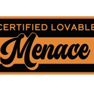 May include: A rectangular sticker with rounded corners, featuring the words "CERTIFIED LOVABLE" above the word "Menace" in a bold, cursive font. The background is black with an orange rectangle.