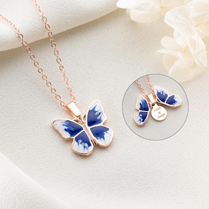 May include: Rose gold butterfly pendant necklace with blue and white enamel wings. The necklace features a delicate chain and a detailed butterfly charm. A smaller circular charm is also visible.