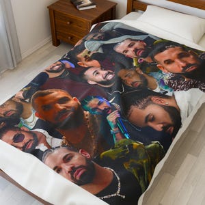 May include: A white blanket featuring a collage of Drake's face in various poses. The blanket has a dark background with multiple images of the rapper. The blanket is on a bed with a white pillow.