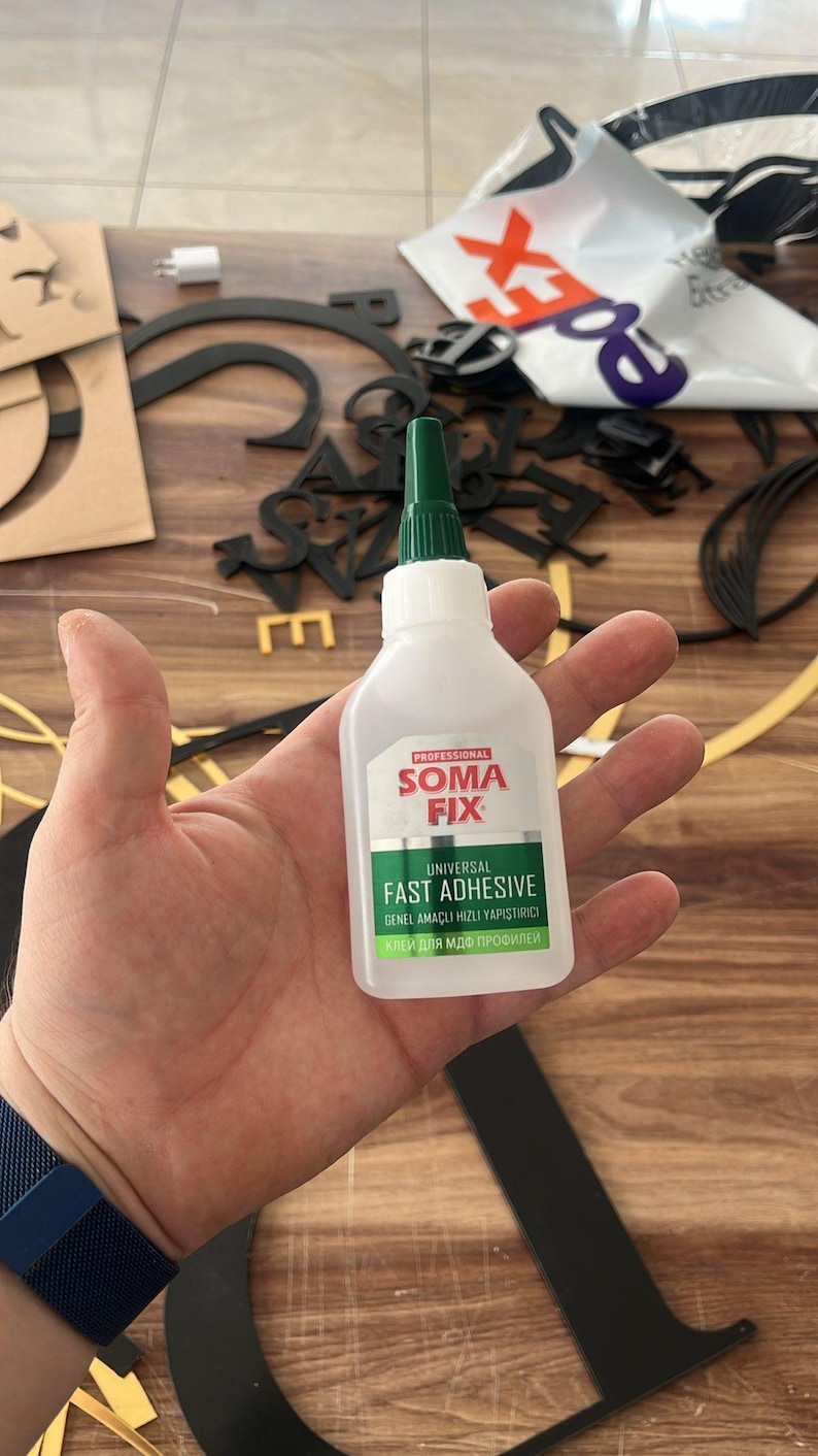May include: A bottle of "Soma Fix" fast adhesive with a green nozzle. The label reads "Universal Fast Adhesive" and includes text in other languages. Black and gold letters are in the background.