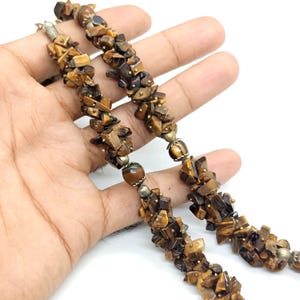 May include: A necklace made of tiger's eye gemstone chips in brown and gold hues. The necklace has a textured design with small metal beads. The gemstones are strung together, creating a natural and earthy aesthetic, suitable for various outfits.