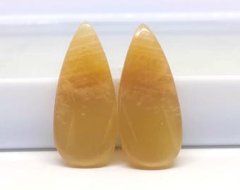 May include: Two polished, teardrop-shaped gemstones. The stones have a translucent, golden-yellow hue with subtle internal veining. The smooth, polished surfaces catch the light, highlighting their natural beauty. These gemstones are ideal for jewelry making.