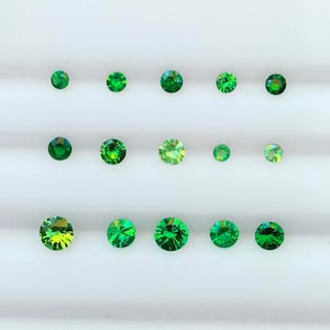 May include: A collection of round, faceted gemstones in shades of green. The gems are arranged in rows on a white surface, highlighting their sparkle and colour variations. The sizes of the gems vary.
