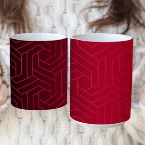 May include: Two ceramic mugs featuring a geometric pattern of interlocking lines. The left mug displays a dark maroon and black color scheme, while the right mug features a vibrant red and bright red design. Both mugs have white interiors.