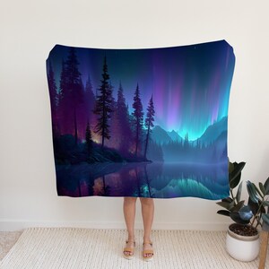 May include: A blanket displaying a digital art landscape with a lake, trees, and mountains under a vibrant aurora borealis. The colour palette includes shades of purple, blue, and green, creating a serene and magical scene.