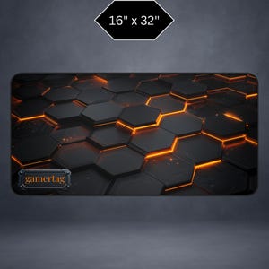 Peut inclure: Tapis de souris de jeu noir et orange avec un motif hexagonal. Le tapis mesure 40,6 x 81,3 cm et comporte le mot "gamertag" dans un petit encadré rectangulaire. Le design a un effet 3D avec des accents orange lumineux.