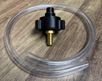 May include: A black plastic fitting with a brass nozzle is connected to a clear, flexible tube. The tube is coiled around the fitting. The items are on a wooden surface.