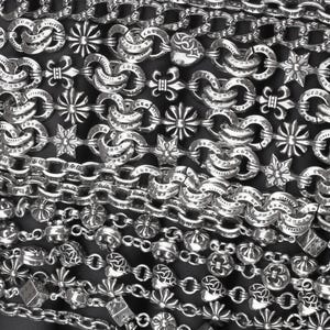 Peut inclure: Une collection de chaînes en argent avec des maillons complexes, incluant des motifs de fleur de lys, d'étoile et de cœur. Les surfaces métalliques sont gravées du texte Chrome Hearts et 925, avec une finition polie et des détails décoratifs.