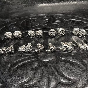 Puede incluir: Un letrero de madera hecho a mano con el texto "Welcome to our home" en un estilo manuscrito. El letrero está pintado de blanco con un acabado envejecido y presenta un diseño floral decorativo. Está diseñado para colgar en la pared.