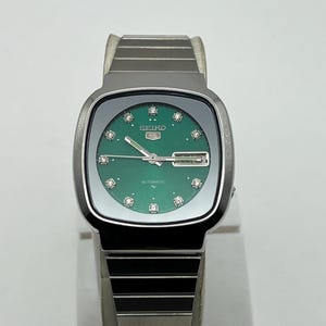 Op de afbeelding: Een vintage Seiko automatisch horloge met een groene wijzerplaat en zilverkleurige kast en band. De wijzerplaat heeft diamant uurmarkeringen en het Seiko-logo. Het horloge wordt gepresenteerd op een wit oppervlak.