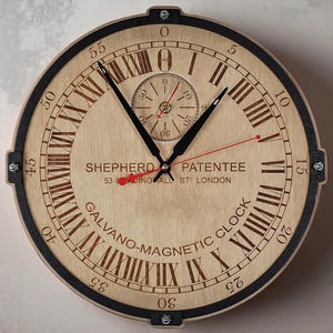 May include: A circular wooden clock featuring Roman numerals and black hands. The clock face has a light wood grain appearance with the text "SHEPHERD PATENTEE" and "GALVANO-MAGNETIC CLOCK". The clock has a black outer rim.