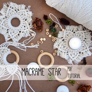 Puede incluir: Decoraciones de estrellas de macramé hechas a mano y anillos de madera, con un carrete de hilo blanco y elementos decorativos. El texto "MACRAME STAR PDF TUTORIAL" es visible. Las estrellas de macramé son de color crema.