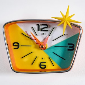 Könnte beinhalten: Eine Retro-Wanduhr mit Stern-Akzent. Das Zifferblatt hat ein geometrisches Design mit gelben, türkisfarbenen und weißen Abschnitten. Die Zeiger sind orange und rosa, und die Zahlen sind schwarz.