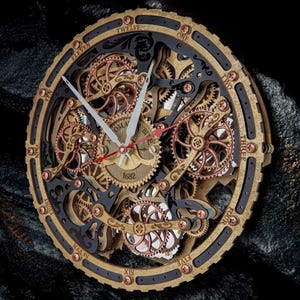 Op de afbeelding: Een gedetailleerde wandklok in steampunk-stijl met zichtbare tandwielen. De klok heeft een goudkleurig frame met zwarte accenten en koperkleurige klinknagels. De wijzers zijn wit en rood, en de wijzerplaat heeft Romeinse cijfers.