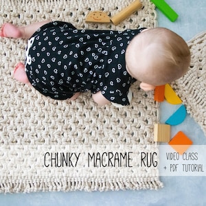 以下が含まれることがあります： 白いハート模様の黒いロンパースを着た赤ちゃんが、クリーム色のマクラメのラグの上にいます。「CHUNKY MACRAME RUG」の文字が見えます。さまざまな形と色の木製ブロックが散らばっています。