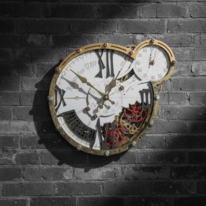May include: Steampunk-style wall clock with a gold-colored frame and exposed gears. The clock face is white with black Roman numerals and the text "Katomy ton 1789". A smaller clock face is attached above the main clock.