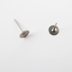 May include: Two silver-colored earring posts with flat, circular backs. The posts are thin and straight, with a small loop at the end. The earring backs are a matte silver finish, and the posts are centered on the backs.