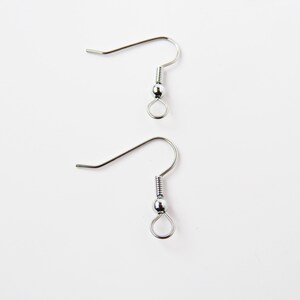 Può includere: Due ganci per orecchini color argento su sfondo bianco. Ogni gancio ha un filo curvo, una molla a spirale, una piccola perla e un anello per attaccare gli orecchini. Ideale per la creazione di gioielli.