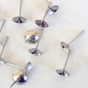May include: Close-up of several silver-colored earring posts with flat, round disc backings. The posts are straight and have a shiny, metallic finish. The earring components are scattered against a white background.