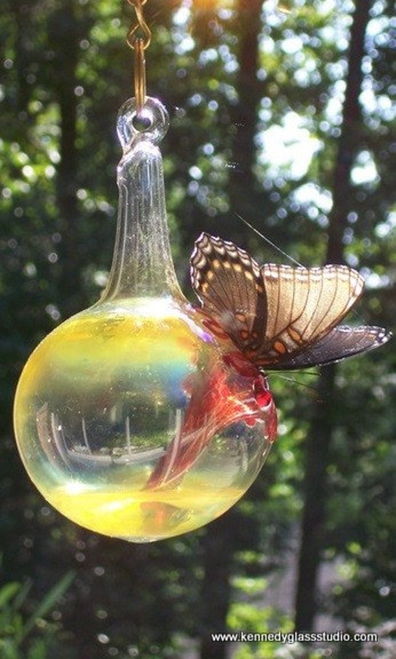May include: A clear glass ornament with a yellow and red butterfly inside. The ornament is hanging from a gold chain.