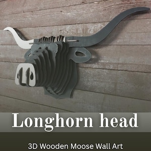 May include: A layered, 3D wooden longhorn head wall art piece. The artwork features a gray head with white accents on the horns and nose. The text "Longhorn head" is displayed below the artwork. The piece is mounted on a wooden plank wall.