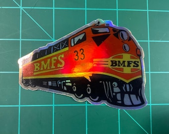 May include: Holographic sticker of a train engine with the text "BMFS" in yellow and the number "33" in red. The train is primarily orange and red with black and yellow accents. The sticker has a reflective, iridescent finish.