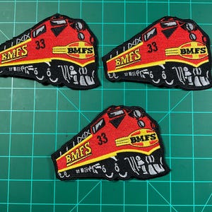 May include: Three embroidered patches with a red and yellow train design. Each patch features the text "BMFS" and the number "33". The patches have a black border and are set against a green background.