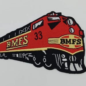 Puede incluir: Parche bordado que representa una locomotora roja con detalles en negro y amarillo. El parche incluye el texto "BMFS" en amarillo y el número "33". El diseño del tren está detallado con ruedas y otros elementos mecánicos.