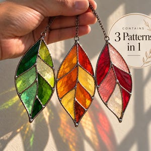 May include: Three stained glass leaf ornaments with metal solder lines, each hanging from a chain. The leaves feature green, yellow, orange, and red glass segments. A circular graphic overlay in the top right corner displays the text Contains 3 Patterns in 1.