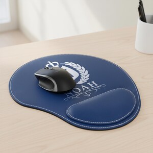 May include: A navy blue mousepad with a white stitched edge and a built-in wrist rest. The mousepad features a white emblem with the name "NOAH". A black and silver wireless mouse sits on the pad.