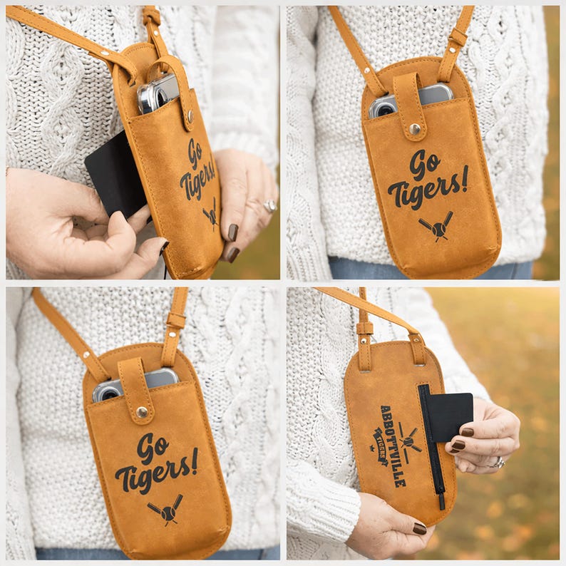 May include: A tan leather crossbody phone case with a shoulder strap. The case has the words "Go Tigers!" and a baseball bat and ball graphic printed on the front. A black card is being inserted into the case.