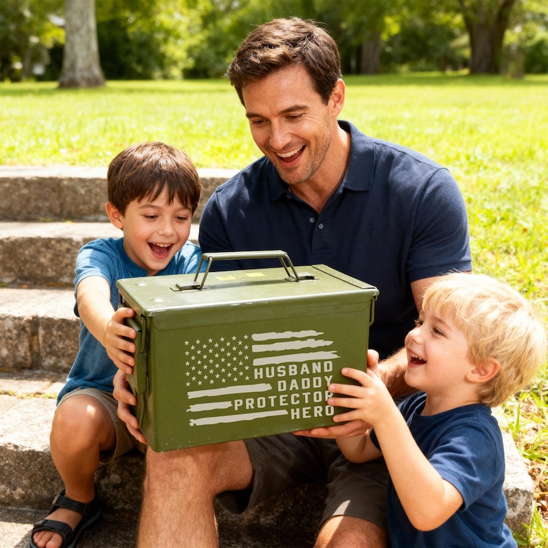 May include: An olive green metal box with a handle, featuring a distressed American flag design and the words "HUSBAND DADDY PROTECTOR HERO" in white. The box is held by a man and two children.