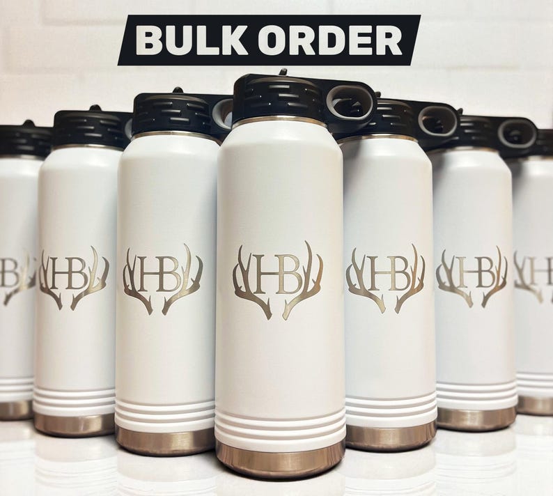 A group of matte white water bottles with black lids standing in rows, each engraved with the monogram letters HB surrounded by antlers.