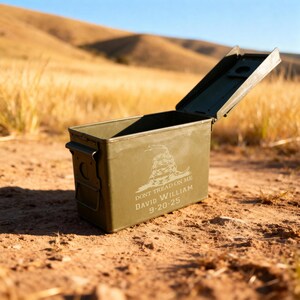 May include: An olive green metal ammunition box with an open lid. The box features the phrase "DON'T TREAD ON ME" and the name "DAVID WILLIAM" with the date "9-20-25" etched on the side. The box is sitting on a dirt surface.