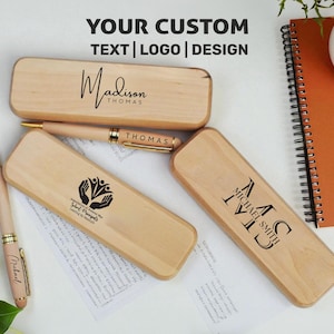 May include: Wooden pen cases with custom text and logos. One case is engraved with "Madison Thomas", another with "Michael Smith", and a third with an organization's logo. A pen with "Thomas" is also visible.