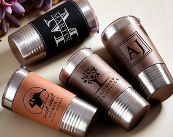 May include: Four stainless steel insulated tumblers with leather sleeves. One black tumbler has the name "MARTIN" with a large "M". Other tumblers are brown with custom logos and text: "AJ", a tree, and "West Coast Women's Golf School".