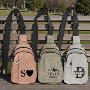 May include: Three personalized sling bags in shades of pink, olive green, and gray. Each bag features a black adjustable strap and a zippered main compartment. The pink bag has an "S" and a heart, the green bag has "KEVIN MILLER", and the gray bag has "D BRYAN".