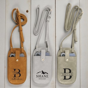 May include: Three leather phone crossbody bags in tan, gray, and beige. Each bag has a long strap and a snap closure. The tan bag has the letter "B" with a floral design and the name "Barbara". The gray bag has the name "Shane Miller" and a mountain graphic. The beige bag has the letter "D" and the name "Bryan".