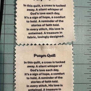 Peut inclure: Deux carrés de tissu blanc cassé avec le texte "Prayer Quilt" et un poème imprimé en noir. Les carrés ont un bord décoratif festonné. Le poème parle de foi, d'espoir et de réconfort.