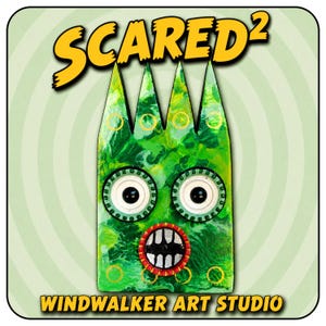 May include: A green, rectangular, three-pointed creature figure with large white eyes, black pupils, and a red-rimmed mouth showing white teeth. The text SCARED2 appears at the top and WINDWALKER ART STUDIO is printed at the bottom.