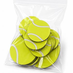 Könnte beinhalten: Eine Sammlung von kreisförmigen, flachen, limonengrünen Scheiben mit einem weißen, geschwungenen Linienmuster, das an Tennisbälle erinnert, verpackt in einem durchsichtigen, wiederverschließbaren Plastikbeutel. Die Scheiben sind gestapelt.