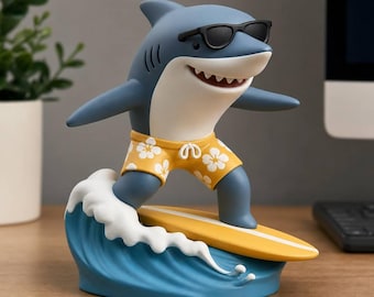May include: A blue shark figurine wearing black sunglasses and yellow swim trunks with a white floral pattern. The shark is standing on a yellow surfboard balanced atop a blue wave with white foam, creating a dynamic surfing scene.