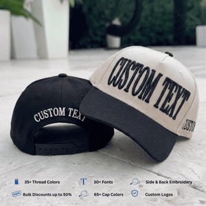 May include: Two baseball caps, one black and one cream, both featuring embroidered text. The cream cap has a black brim and the words CUSTOM TEXT in black. The black cap has white text reading CUSTOM TEXT and an adjustable snapback closure.