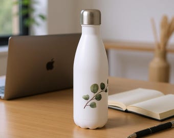 以下が含まれることがあります： 銀色のキャップとユーカリの葉の植物柄が付いた白い断熱ウォーターボトル。 ボトルは、ラップトップ、開いたノート、ペンが置かれた木製の机の上にあります。