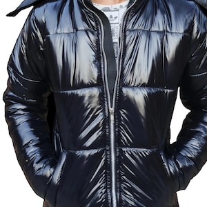 May include: A shiny black puffer jacket with a hood and a full-length zipper. The jacket has a quilted design and two front pockets. The model is wearing a white t-shirt underneath. The jacket is a stylish outerwear option.