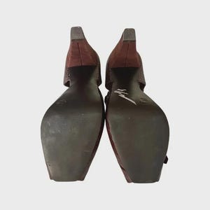 May include: Pair of burgundy-colored women's heels with a textured, snakeskin-like pattern. The shoes have a square toe and a block heel. The soles are dark brown. The heels are approximately 3 inches high.