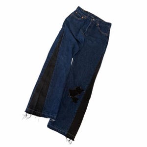 May include: Dark wash denim jeans with black side stripes and star-shaped patches on the knee. The jeans have a classic five-pocket design and a frayed hem. A stylish and unique addition to any wardrobe.