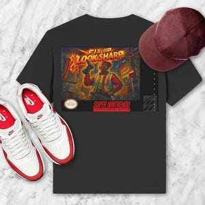 Puede incluir: Camiseta negra con un gráfico que presenta a un hombre sosteniendo un arma, las palabras "FIX UP LOOK SHARP" y "SUPER NINTENDO ENTERTAINMENT SYSTEM". Una gorra de béisbol burdeos y zapatillas blancas y rojas completan el conjunto.