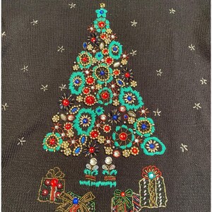 以下が含まれることがあります： 黒いセーターに刺繍されたクリスマスツリーのデザイン。ツリーは、ターコイズ、赤、青、金の装飾で飾られています。プレゼントは木の根元に刺繍され、星の形がセーター全体に散らばっています。